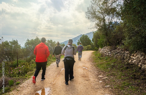 Fototapeta People walking along a path, near the Sierra de Bernia mountains, on a spring day, with cloudy skies.