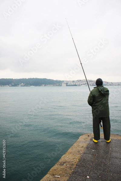 Fototapeta A lone mid age fisherman with yellow boots fishing on the Bosphorus shore in Istanbul.