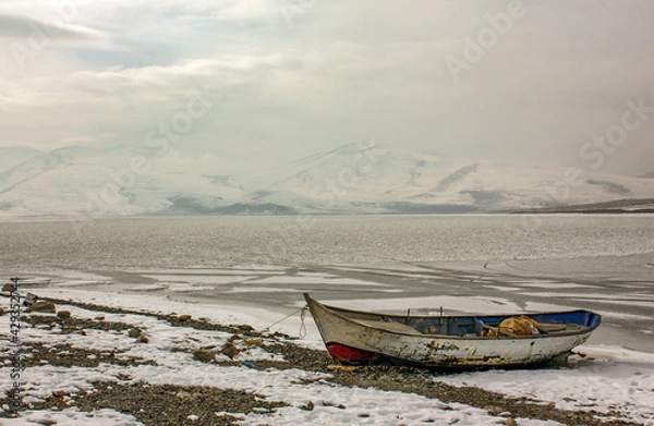 Fototapeta A worn-out old fishing boat tied up on the beach on a frozen lake in winter, Çıldır Lake, Kars, Turkey.