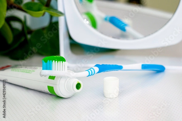 Obraz an open tube of toothpaste a toothbrush with applied toothpaste and a mirror on the dressing table