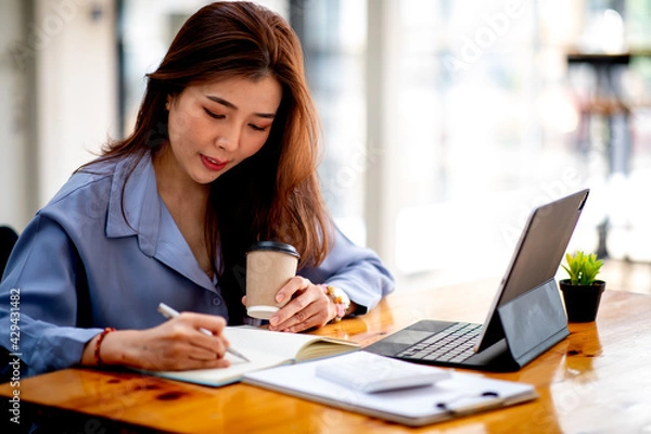 Fototapeta Business young female working analyzing investment charts on calculator and tablet,Work From Home concept.