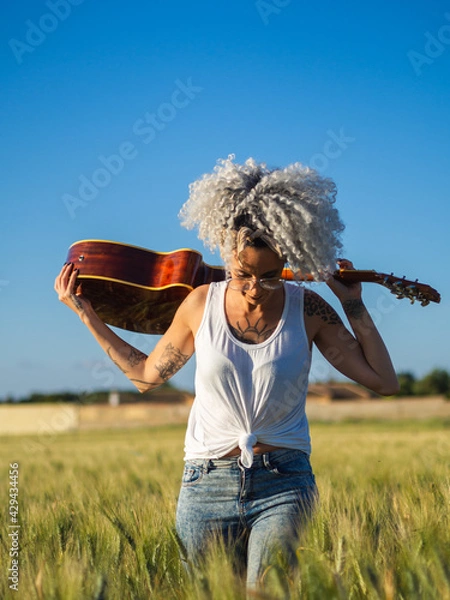 Fototapeta Mujer joven con una guitarra en un campo de trigo 