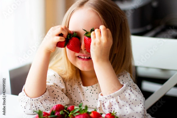 Fototapeta  Cute little girl eating fresh strawberry in the kitchen. Healthy vitamin snack for kids. Ripe fresh berries. Harvest season. Natural vitamins .