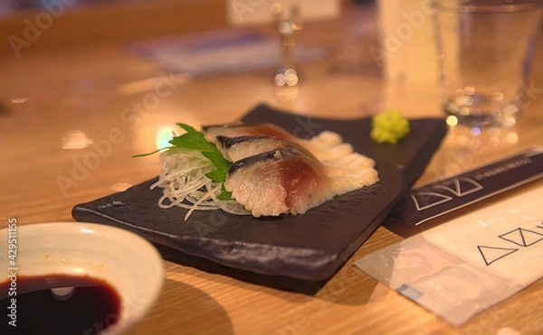 Obraz Selective focus on a small plate of thinly-sliced mackerel sashimi, garnished with wasabi, a shiso leaf, and chopped daikon radish
