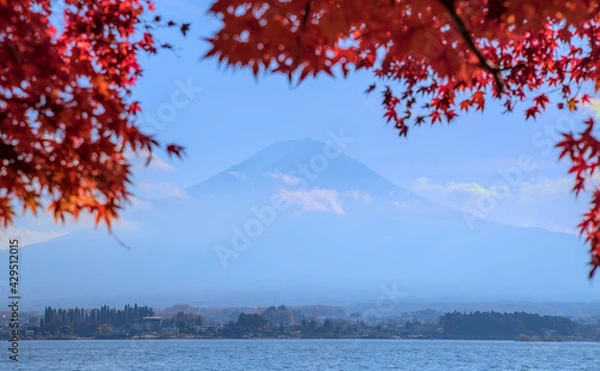 Obraz Hazy daytime view of Mount Fuji and Lake Kawaguchi, framed by red maple leaves and under a blue sky
