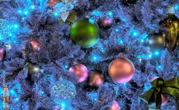 Obraz Close-up view of a number of colorful Christmas ornaments on a blue Christmas tree, illuminated by blue lights