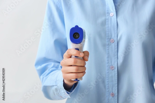 Fototapeta Woman with infrared thermometer on light background, closeup