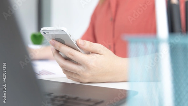 Fototapeta Asian female employees are analyzing market data via smartphones and have laptops to calculate the company's finances In a private office at home, Working at home and new normal concept.
