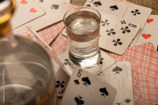 Fototapeta Playing cards, a glass of vodka and a decanter of vodka on a table covered with coarse burlap.