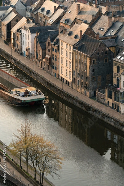 Obraz A barge crosses the Sambre next to houses at sunset.