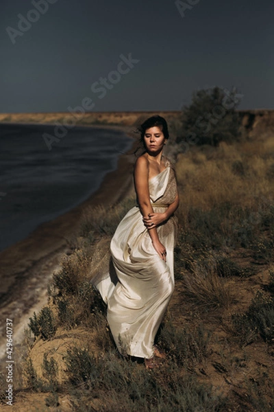 Obraz A beautiful girl in a stilted suit stands on a mountain above the sea, a lake on a sunny day.