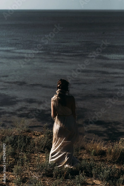 Obraz A beautiful girl in a stilted suit stands on a mountain above the sea, a lake on a sunny day.