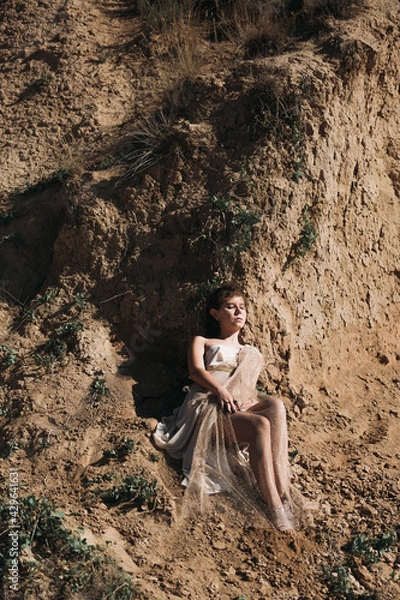 Obraz A beautiful girl in a stylized suit sits on a mountain above the sea, lake on a sunny day.