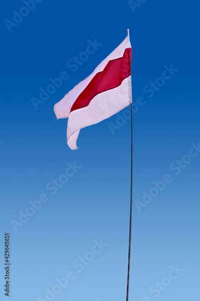 Obraz Isolated waving Belarusian national flag on blue sky background. White-red-white flag. A symbol of peaceful protests in Belarus against the dictatorship after presidential elections.