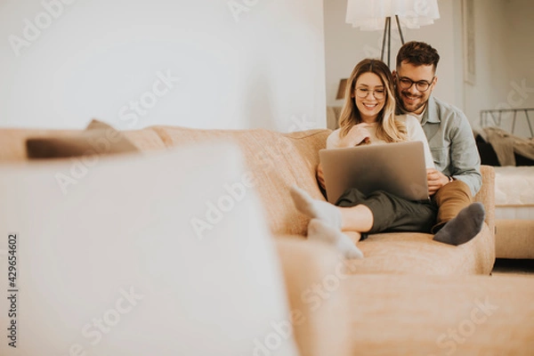 Obraz Young couple using laptop together while sitting on sofa at home