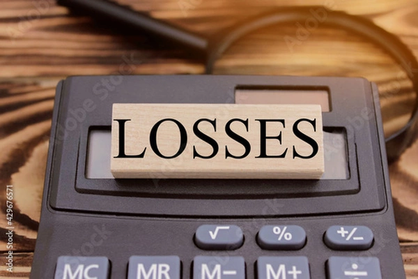 Fototapeta loss is written on wooden cubes, the cubes are on a stack of books on the table, the background is light
