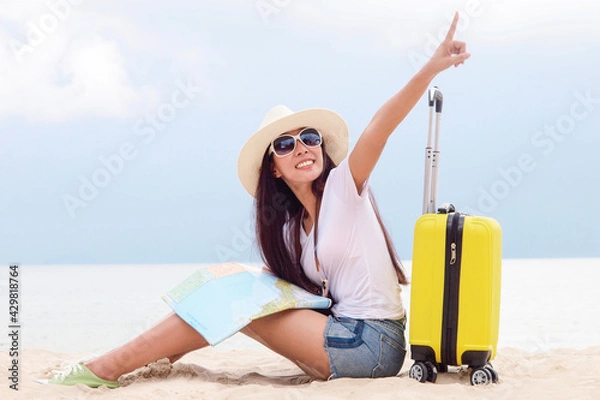 Fototapeta Summer Party. Traveler and tourism woman travel in summer on the beach and white sand. Asian is looking at map with yellow suitcase. On working in vacation concept.