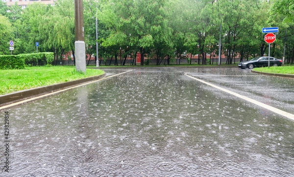 Fototapeta Heavy rain with hail in the city on a summer day. Large puddles on the roadway. Wet road with puddles of spray.