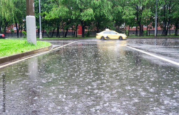Fototapeta Heavy rain with hail in the city on a summer day. Large puddles on the roadway. Wet road with puddles of spray.