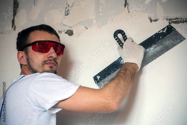 Fototapeta work on finishing the walls with mixtures of plaster and putty when building a house. builder worker plastering facade of high-rise building with putty knife. leveling stone walls