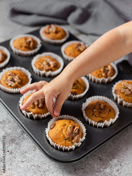 Fototapeta Banana muffins. Super healthy delicious muffins made from ripe bananas with the addition of chopped walnuts. A child's hand wants to take them