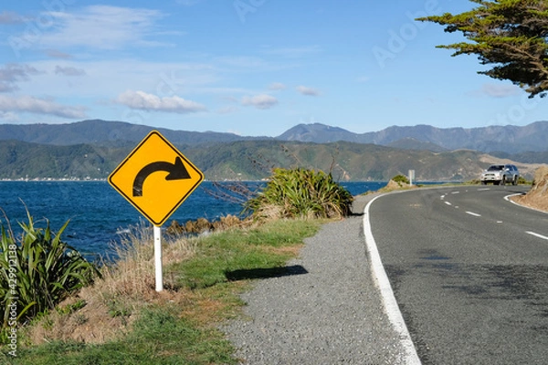 Obraz Sign warning of a upcoming bend on an ocean road