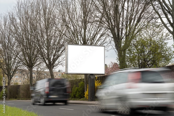 Obraz Advertisement billboard panel for a mockup. Empty template for an ad next to a street with moving cars. Space for a commercial poster in the inner city. White display in a public area.