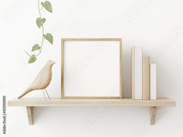 Obraz Small square wooden frame mockup in scandi style interior with trailing green plant, bird, pile of books and shelf on empty neutral white wall background. 3d rendering, illustration