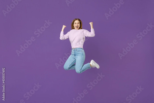 Fototapeta Full length young excited overjoyed happy woman 20s wearing purple knitted sweater jump high do winner gesture clench fist isolated on violet color background studio portrait People lifestyle concept.