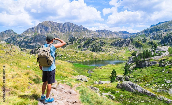 Fototapeta Young traveler man with a backpacker standing on an alpine mountain trail with a lake. Circo de Saboredo, Aran Valley, Catalan Pyrenees, Catalonia, Spain, Europe.