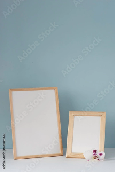 Fototapeta Spring still life. Two wooden portrait frames mockup on white table with orchid flower. Blue wall background.