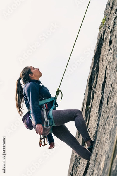 Obraz Female climber looks up tiredly hanging from climbing rope in safety.