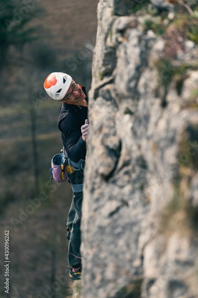 Obraz Man climbs vertical wall with helmet with blurred rock in the foreground.