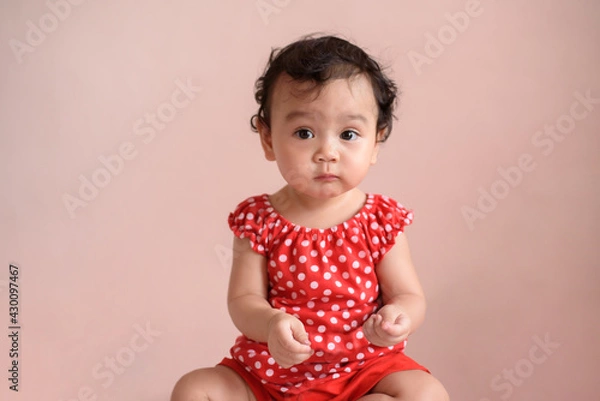 Obraz Portrait of a cute little Asian baby girl wear red dress look at camera isolated on background, baby expression concept