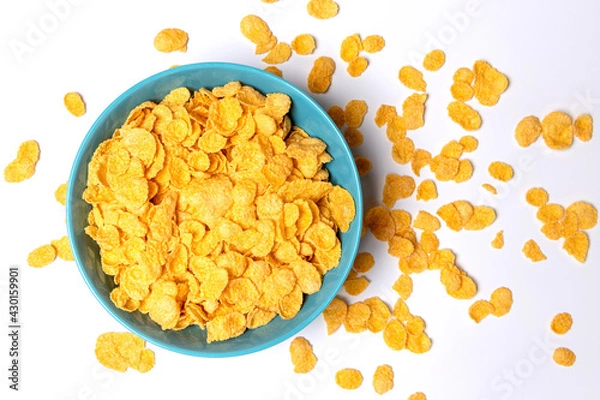 Fototapeta Cornflakes in a blue cup isolated on a light background. Scattered cornflakes lie nearby. Top view.