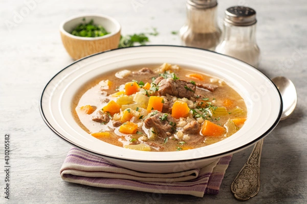 Fototapeta Beef and barley soup with celery, carrot and onion in plate on concrete background
