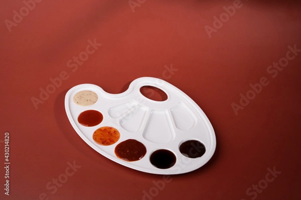 Obraz A palette of flavors. On a red background there is a white palette in which sauces are poured instead of paint: cheese, garlic, barbecue, sweet and sour.Food is art. Sauces for food. An unusual pitch.