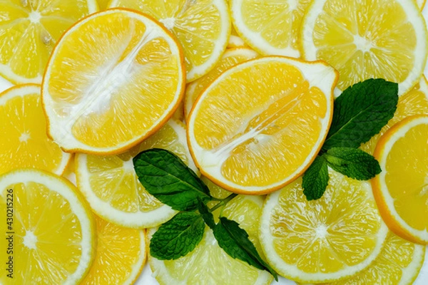 Fototapeta halves and slices of fresh juicy bright yellow lemons with mint leaves, spread out as a background, taken close-up