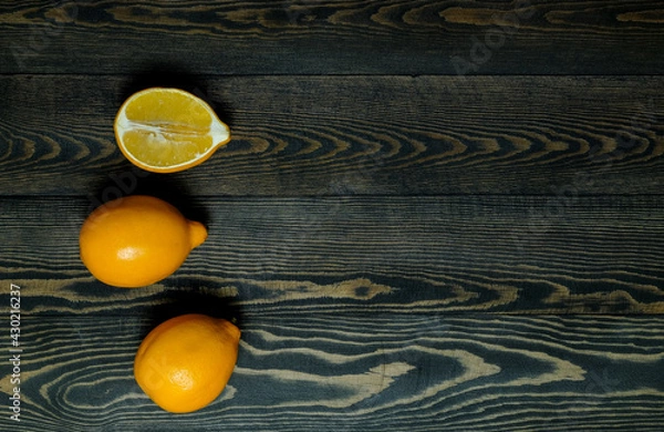 Fototapeta two whole lemons and one half lemon on a dark, coarse wooden background from boards
