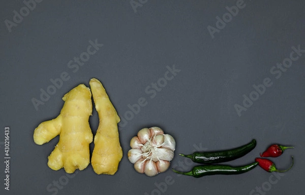 Fototapeta two roots of juicy fresh ginger, garlic head, sharp red and green peppers on a gray background, photographed close-up