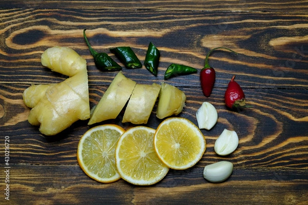 Fototapeta fresh juicy ginger cut into slices, lemon slices, garlic slices, green and red hot peppers on a dark, coarse wooden background