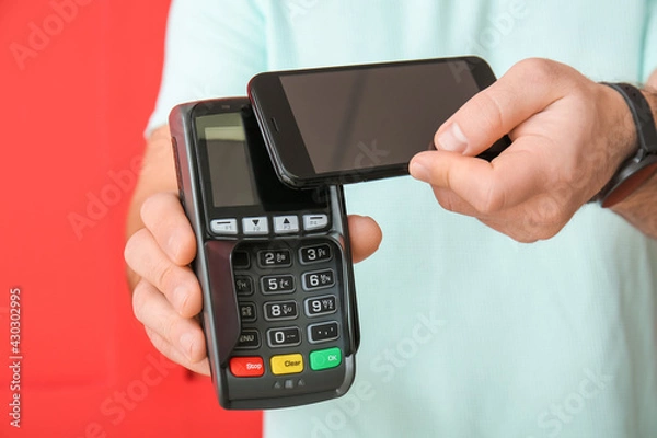 Obraz Man with payment terminal and mobile phone on color background, closeup