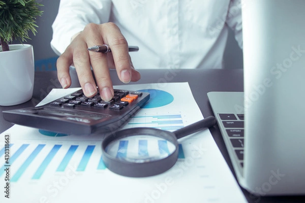 Fototapeta business people who use a calculator with financial concepts, spreadsheet data, business people use their fingers to compute calculations.