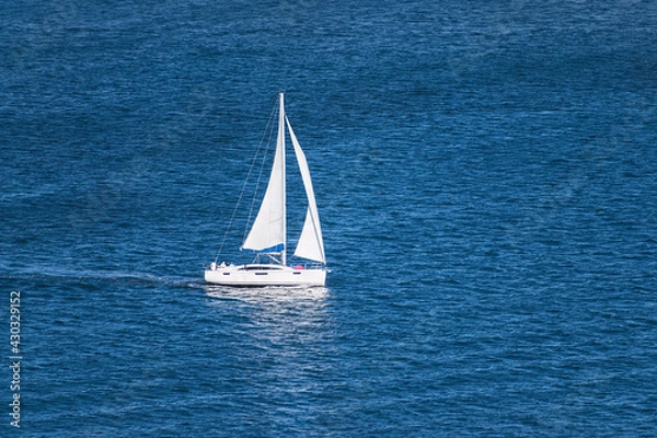 Obraz aerial view of a generic white sailboat with two sails sailing on very calm water in the San Diego Bay in Southern California surrounded by small ripples and swells