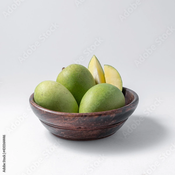 Fototapeta natural raw or green mangos or aam in a wooden bowl with green mango leaves on a white background useful for packaging or editorial purpose