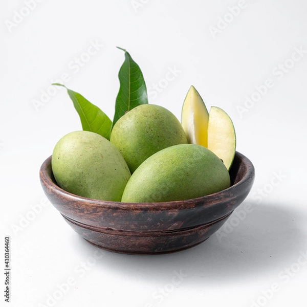 Fototapeta natural raw or green mangos or aam in a wooden bowl with green mango leaves on a white background useful for packaging or editorial purpose