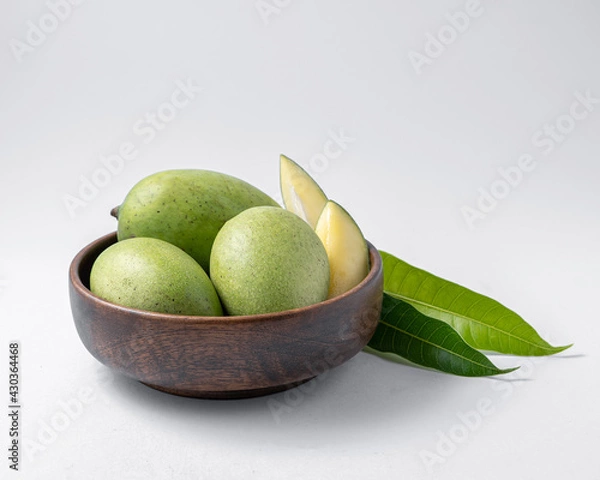 Fototapeta natural raw or green mangos or aam in a wooden bowl with green mango leaves on a white background useful for packaging or editorial purpose