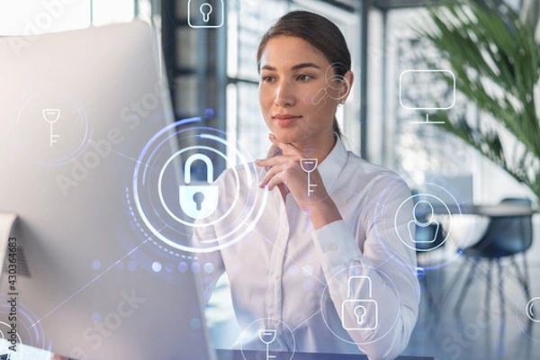 Fototapeta Attractive businesswoman in white shirt at workplace working with laptop to defend customer cyber security. Concept of clients information protection. Padlock hologram over office background.