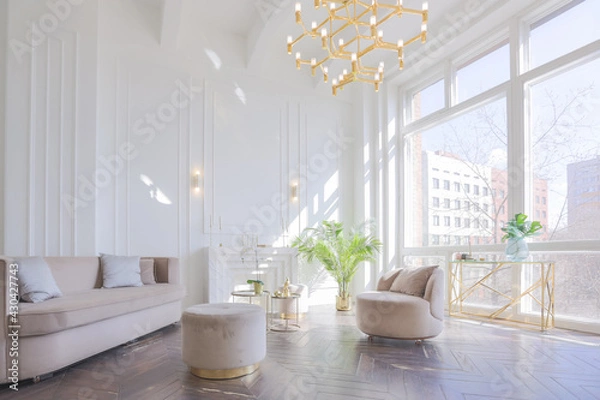 Obraz very light and bright interior of luxurious cozy living room with chic soft beige furniture with gold metallic elements, huge window to the floor and wooden parquet