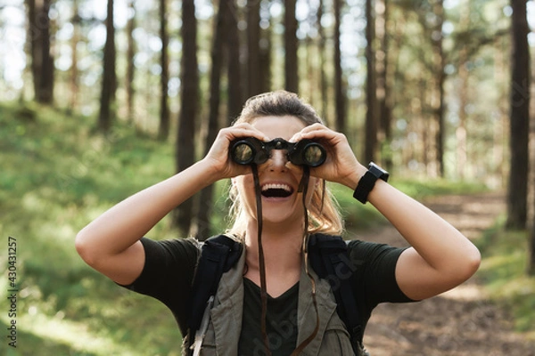 Fototapeta Female hiker is using binoculars for bird watching in green forest